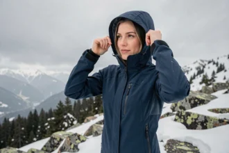 Femme portant une veste technique de montagne haut de gamme sur un sommet rocheux enneigé en hiver